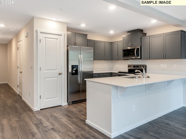 kitchen featuring gray cabinetry, dark wood-type flooring, stainless steel appliances, kitchen peninsula, and a breakfast bar area