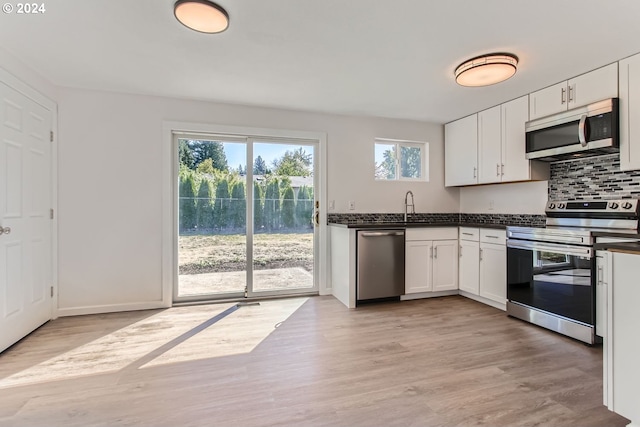 kitchen featuring decorative backsplash, appliances with stainless steel finishes, white cabinetry, light wood-type flooring, and sink