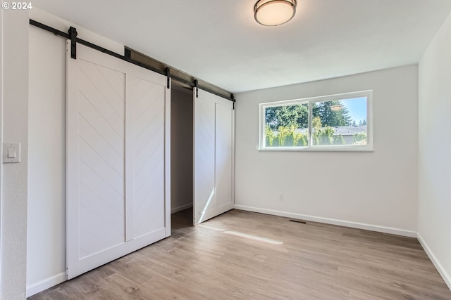 unfurnished bedroom featuring a closet, light wood-type flooring, and a barn door