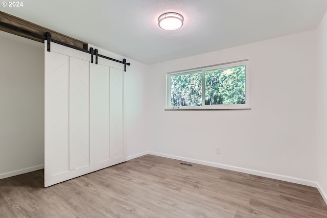 unfurnished bedroom featuring a closet, a barn door, and light wood-type flooring