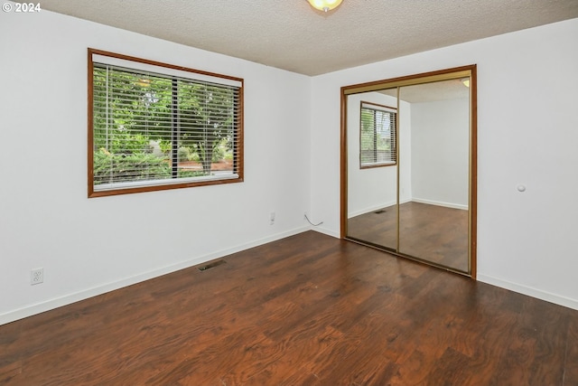 spare room featuring dark wood-type flooring, a textured ceiling, and a healthy amount of sunlight