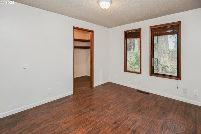 unfurnished bedroom featuring a textured ceiling, a closet, dark wood-type flooring, and a walk in closet