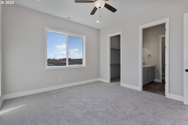 unfurnished bedroom featuring ensuite bath, carpet flooring, ceiling fan, a spacious closet, and a closet