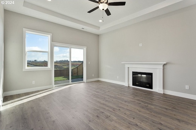 unfurnished living room featuring a raised ceiling, ceiling fan, and wood-type flooring