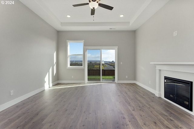 unfurnished living room featuring hardwood / wood-style floors, a tray ceiling, and ceiling fan