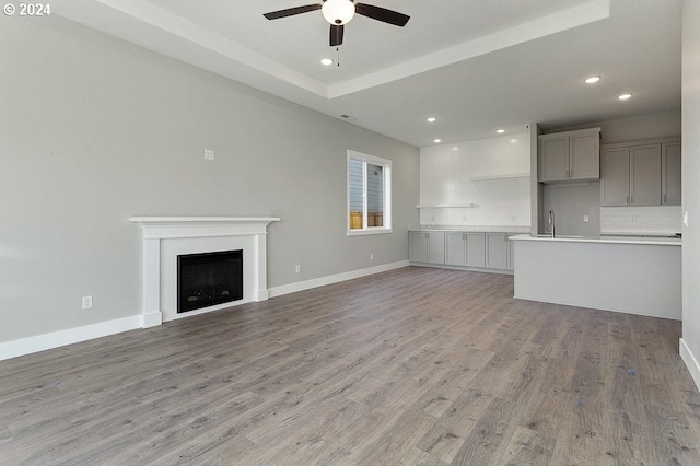 unfurnished living room with light wood-type flooring, a tray ceiling, and ceiling fan