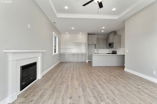 unfurnished living room featuring a raised ceiling, ceiling fan, and light hardwood / wood-style floors