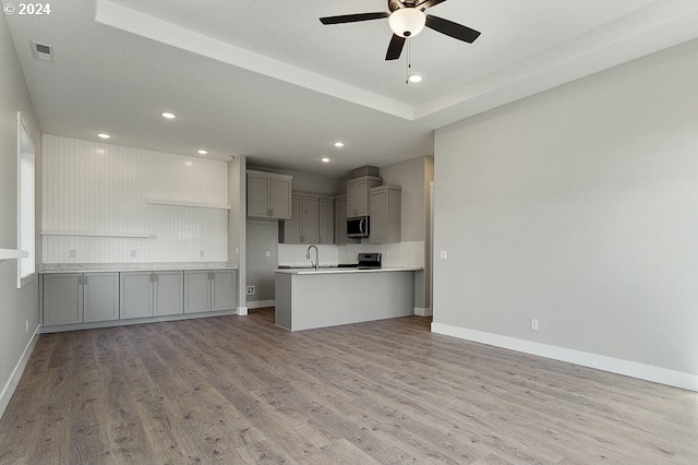 kitchen with kitchen peninsula, light wood-type flooring, stainless steel appliances, ceiling fan, and gray cabinets