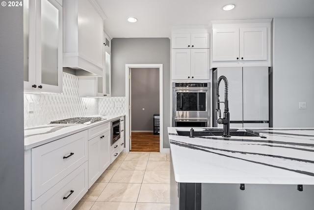 kitchen with white cabinets, light tile patterned floors, tasteful backsplash, appliances with stainless steel finishes, and light stone countertops