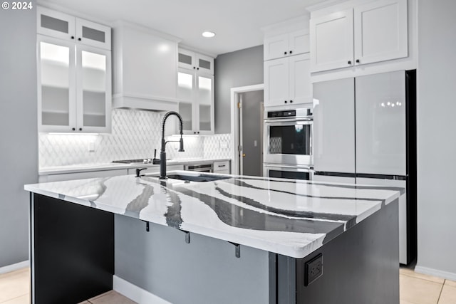 kitchen with tasteful backsplash, sink, white cabinets, a kitchen island with sink, and light stone countertops