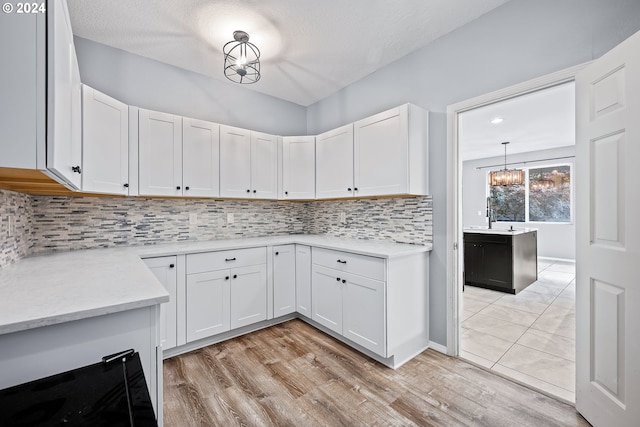 kitchen with white cabinets, pendant lighting, a textured ceiling, a chandelier, and light hardwood / wood-style floors