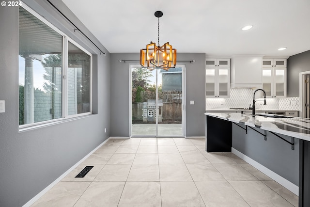 kitchen with a healthy amount of sunlight, tasteful backsplash, pendant lighting, and white cabinets