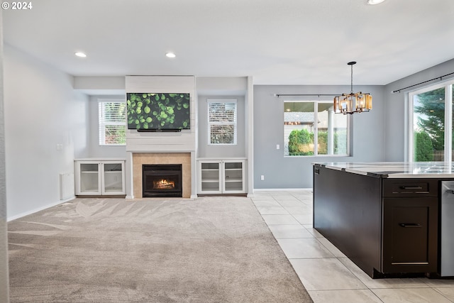 unfurnished living room with an inviting chandelier, a tiled fireplace, and light carpet