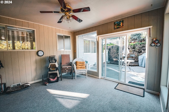 sitting room with carpet floors, wood walls, and ceiling fan