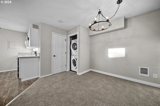 clothes washing area featuring dark carpet, a notable chandelier, heating unit, and stacked washer and dryer