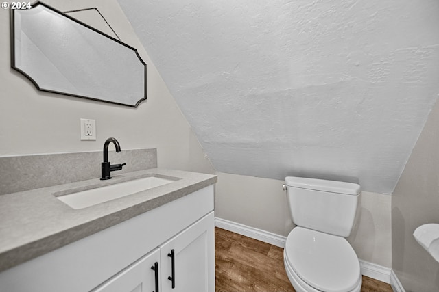 bathroom with vaulted ceiling, hardwood / wood-style flooring, vanity, and toilet