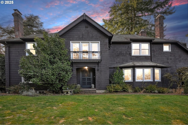 view of front facade featuring a chimney, a yard, and a balcony