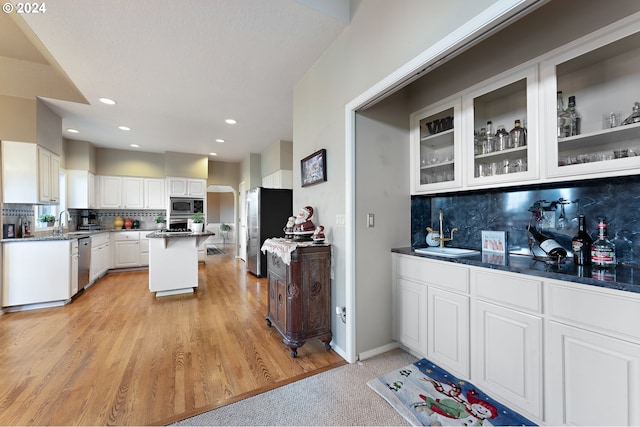 kitchen featuring white cabinets, light hardwood / wood-style flooring, tasteful backsplash, a kitchen island, and stainless steel appliances