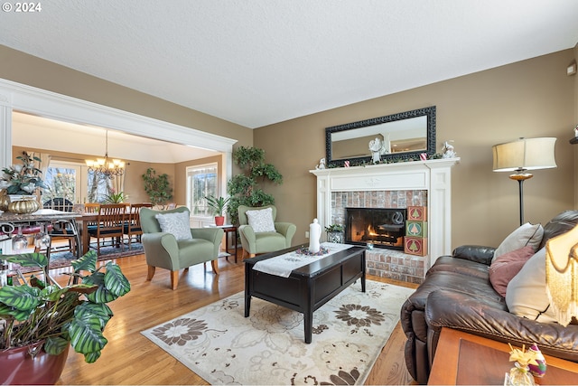 living room featuring light wood-type flooring, a fireplace, a wealth of natural light, and an inviting chandelier