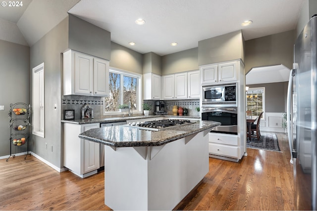 kitchen featuring a center island, stainless steel appliances, white cabinetry, and dark stone counters