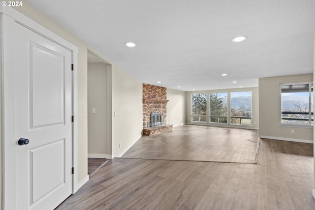 unfurnished living room with a textured ceiling, hardwood / wood-style flooring, and a brick fireplace