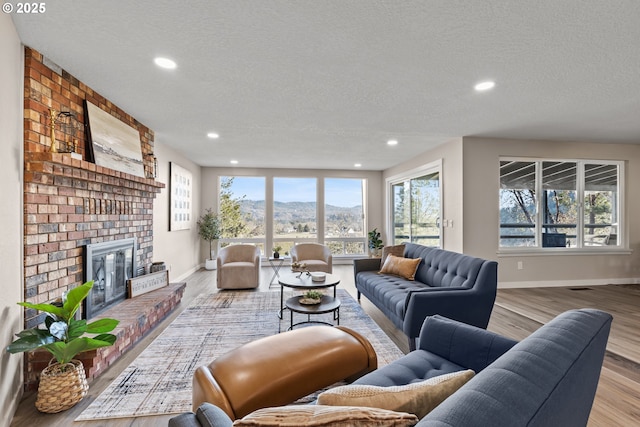 living room featuring a mountain view, light hardwood / wood-style flooring, a fireplace, and a textured ceiling