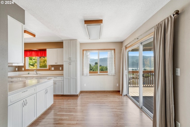 kitchen with white cabinetry, sink, light hardwood / wood-style flooring, and a textured ceiling