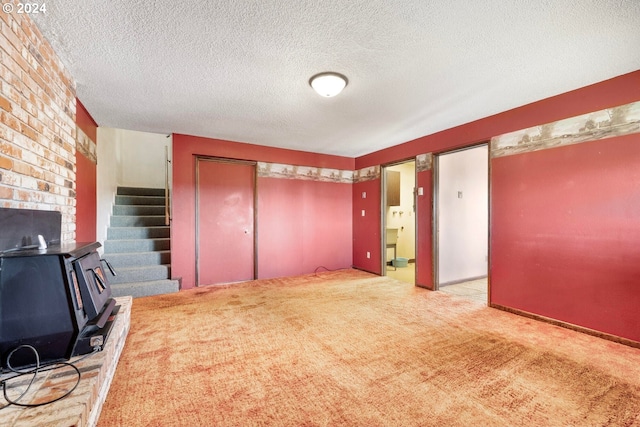 unfurnished living room featuring a wood stove, light colored carpet, and a textured ceiling