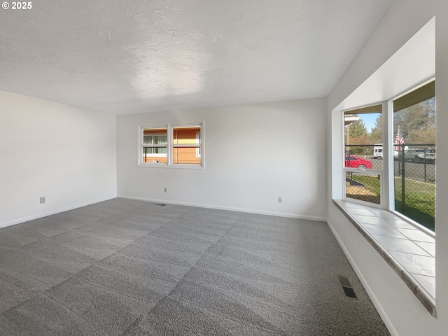 spare room with visible vents, a healthy amount of sunlight, a textured ceiling, and dark carpet