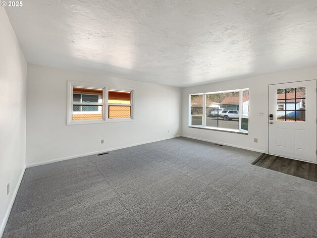 unfurnished room with a textured ceiling, dark carpet, visible vents, and a healthy amount of sunlight