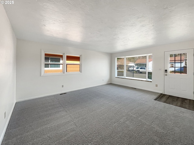 interior space with visible vents, baseboards, a textured ceiling, and dark carpet