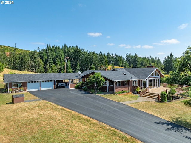 ranch-style home featuring aphalt driveway, an attached garage, a view of trees, and a front lawn