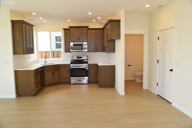 kitchen with light hardwood / wood-style flooring, tasteful backsplash, stainless steel appliances, and sink