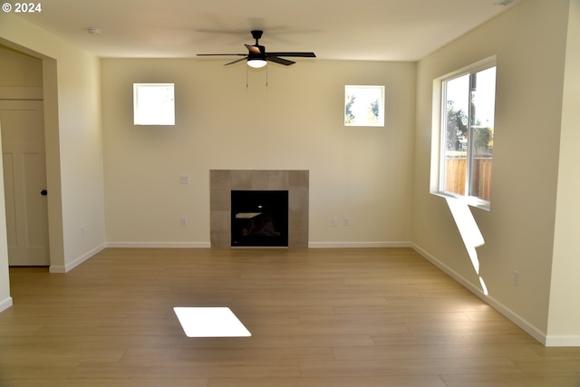 unfurnished living room with a wealth of natural light, light hardwood / wood-style flooring, a tile fireplace, and ceiling fan