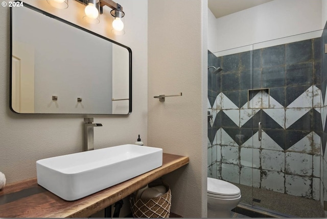 bathroom featuring a stall shower, toilet, a textured wall, and a sink