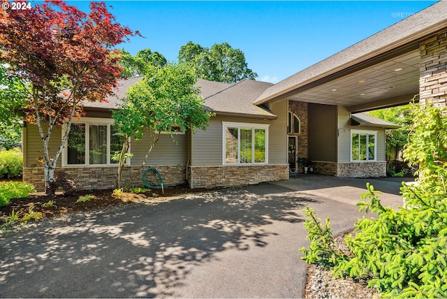 view of front of property featuring stone siding, driveway, and roof with shingles