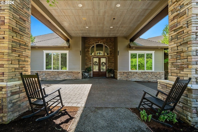 view of exterior entry featuring a patio, french doors, stone siding, and a shingled roof