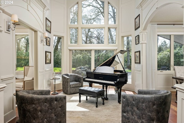 sitting room with arched walkways, a decorative wall, a towering ceiling, and wood finished floors