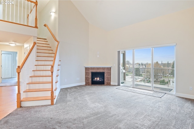 unfurnished living room featuring a tile fireplace, carpet floors, and high vaulted ceiling