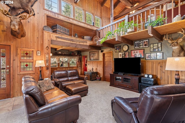 living room featuring carpet, wooden walls, beam ceiling, and a towering ceiling