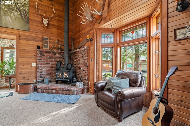 carpeted living room featuring a towering ceiling, wood walls, a wood stove, and plenty of natural light