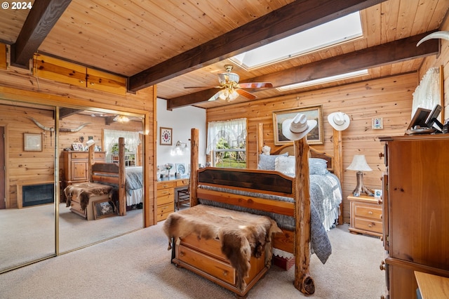 carpeted bedroom featuring wooden walls, ceiling fan, beamed ceiling, and a skylight