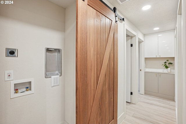 hallway featuring a barn door, light hardwood / wood-style floors, and a textured ceiling