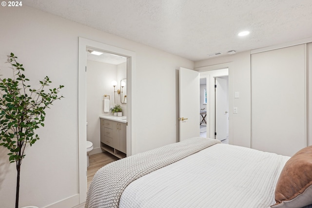 bedroom with ensuite bathroom, light hardwood / wood-style floors, and a textured ceiling