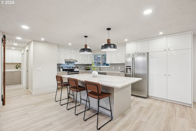 kitchen with a kitchen island, light wood-type flooring, appliances with stainless steel finishes, hanging light fixtures, and white cabinets