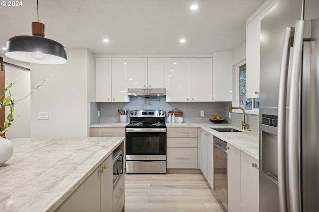 kitchen with stainless steel appliances, white cabinetry, light stone countertops, hanging light fixtures, and sink