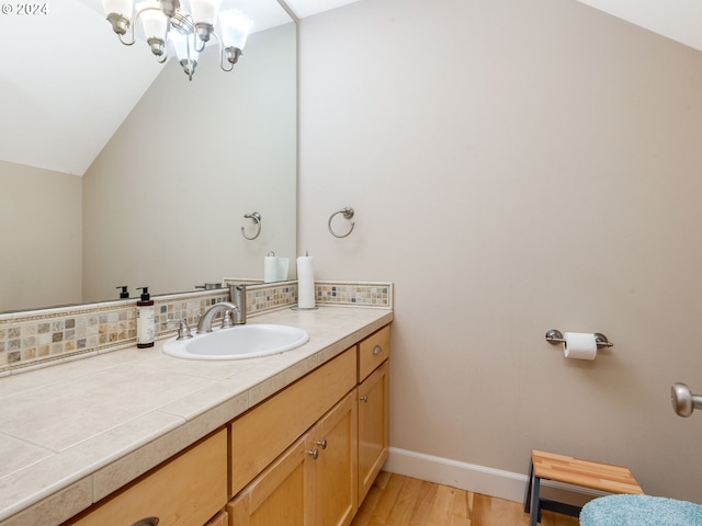 bathroom with vanity, wood-type flooring, backsplash, and vaulted ceiling