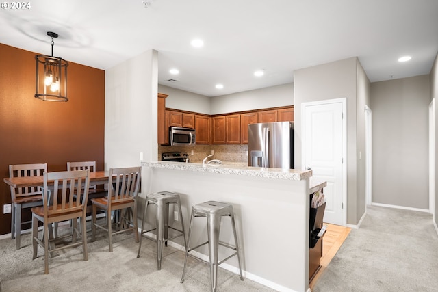 kitchen featuring kitchen peninsula, appliances with stainless steel finishes, light colored carpet, and hanging light fixtures