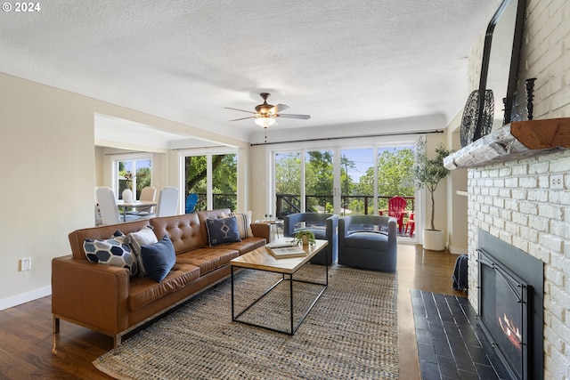 living room with a wealth of natural light, ceiling fan, dark wood-type flooring, and a brick fireplace