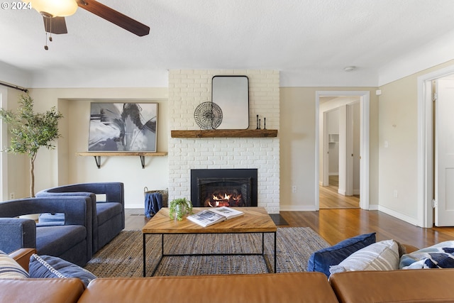 living room featuring a textured ceiling, a brick fireplace, ceiling fan, and dark wood-type flooring